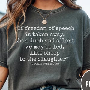 May include: A charcoal gray short-sleeve t-shirt featuring white text that reads: "If freedom of speech is taken away, then dumb and silent we may be led, like sheep to the slaughter" followed by the attribution "-GEORGE WASHINGTON".