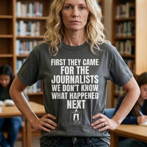 May include: A charcoal grey short-sleeved t-shirt featuring white text that reads: FIRST THEY CAME FOR THE JOURNALISTS WE DON'T KNOW WHAT HAPPENED NEXT, with a graphic of a press badge below the text.