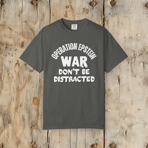 Anti War with Iran Operation Epstein Don't be Distracted. This garment speaks with conviction. A heavyweight, garment-dyed tee printed with a bold, protest-forward message that draws attention without shouting. The soft, broken-in hand of garment dyeing and the relaxed fit make it comfortable for long days at rallies, vigils, or standing on the street holding a sign. Worn by someone who wants their stance to be seen and felt, it layers easily under a jacket or stands alone as a statement piece.