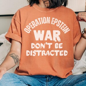 Anti War with Iran Operation Epstein Don't be Distracted. This garment speaks with conviction. A heavyweight, garment-dyed tee printed with a bold, protest-forward message that draws attention without shouting. The soft, broken-in hand of garment dyeing and the relaxed fit make it comfortable for long days at rallies, vigils, or standing on the street holding a sign. Worn by someone who wants their stance to be seen and felt, it layers easily under a jacket or stands alone as a statement piece.