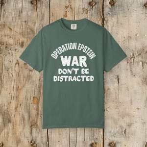Anti War with Iran Operation Epstein Don't be Distracted. This garment speaks with conviction. A heavyweight, garment-dyed tee printed with a bold, protest-forward message that draws attention without shouting. The soft, broken-in hand of garment dyeing and the relaxed fit make it comfortable for long days at rallies, vigils, or standing on the street holding a sign. Worn by someone who wants their stance to be seen and felt, it layers easily under a jacket or stands alone as a statement piece.
