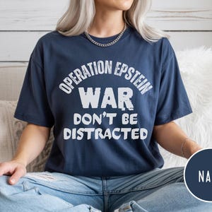Anti War with Iran Operation Epstein Don't be Distracted. This garment speaks with conviction. A heavyweight, garment-dyed tee printed with a bold, protest-forward message that draws attention without shouting. The soft, broken-in hand of garment dyeing and the relaxed fit make it comfortable for long days at rallies, vigils, or standing on the street holding a sign. Worn by someone who wants their stance to be seen and felt, it layers easily under a jacket or stands alone as a statement piece.