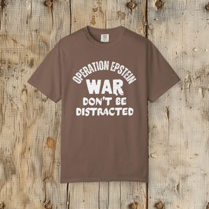 Anti War with Iran Operation Epstein Don't be Distracted. This garment speaks with conviction. A heavyweight, garment-dyed tee printed with a bold, protest-forward message that draws attention without shouting. The soft, broken-in hand of garment dyeing and the relaxed fit make it comfortable for long days at rallies, vigils, or standing on the street holding a sign. Worn by someone who wants their stance to be seen and felt, it layers easily under a jacket or stands alone as a statement piece.