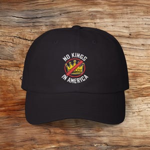 May include: Black baseball cap with an embroidered design of a crown with a red line through it and the text "NO KINGS IN AMERICA".