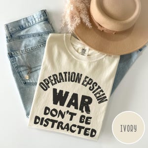 Anti War with Iran Operation Epstein Don't be Distracted. This garment speaks with conviction. A heavyweight, garment-dyed tee printed with a bold, protest-forward message that draws attention without shouting. The soft, broken-in hand of garment dyeing and the relaxed fit make it comfortable for long days at rallies, vigils, or standing on the street holding a sign. Worn by someone who wants their stance to be seen and felt, it layers easily under a jacket or stands alone as a statement piece.