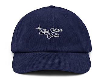 May include: A navy blue corduroy baseball cap with white embroidered text that reads "Ave Maris Stella" and a small star above the text.