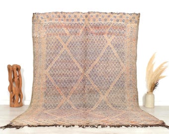 May include: A large, rectangular rug with a diamond pattern in shades of beige, blue, and orange. The rug has a fringe along the bottom edge and is displayed against a white wall. The rug is a decorative home decor item.