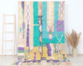 May include: A colourful Moroccan rug with geometric patterns in shades of purple, blue, yellow, and white. The rug has a fringed edge and is made of wool.
