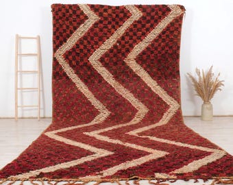 Peut inclure: Un grand tapis rectangulaire avec un motif géométrique. Le tapis présente un fond rouge et marron avec un motif en zigzag de couleur beige clair. Le tapis a une frange le long du bord inférieur.