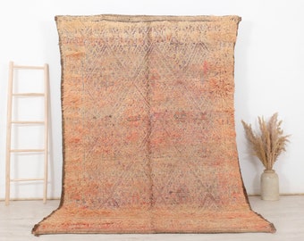 May include: A large, rectangular, beige and pink Moroccan rug with a geometric pattern. The rug has a fringe border and is made of wool.