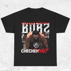 May include: Black t-shirt featuring a graphic of a man with two wolves and the text "Khamzat Chimaev BORZ" in white and red. The shirt also has the text "THE CHECHEN WOLF".
