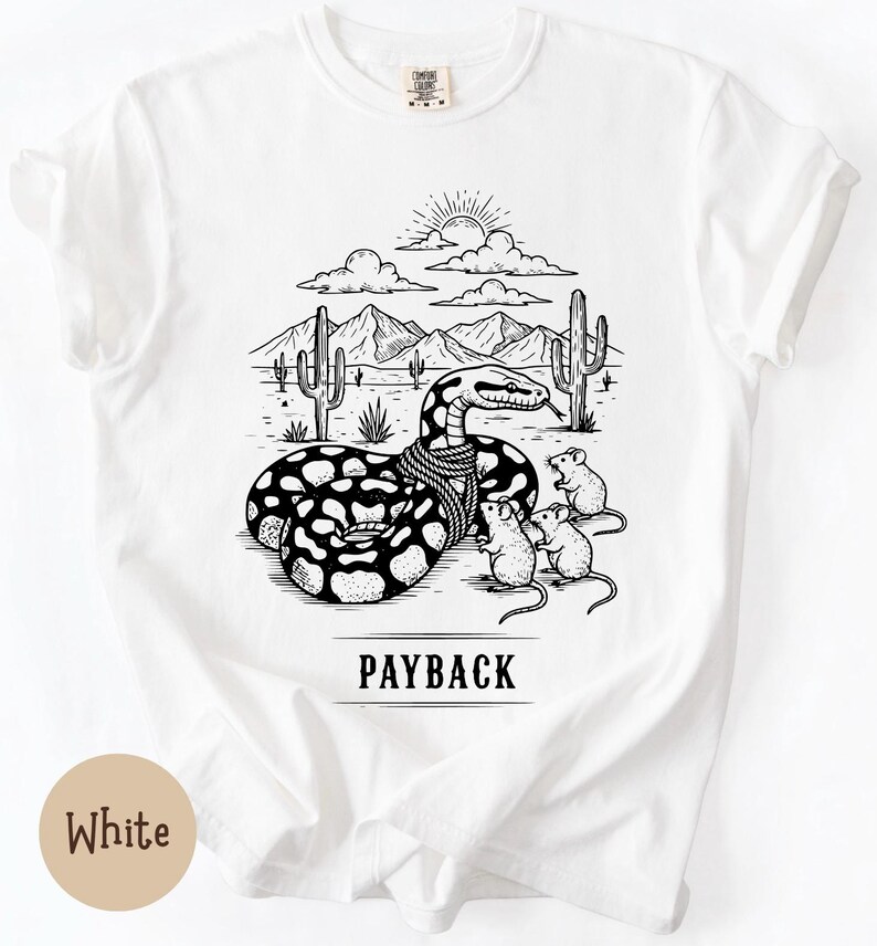 May include: White t-shirt featuring a black and white illustration of a snake with a scarf, mice, and a desert scene. The text "PAYBACK" is printed below the image. The shirt is made of a soft material.