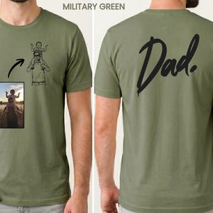 May include: A military green t-shirt featuring a custom line art illustration of a person carrying a child on their shoulders on the front, alongside a small photographic reference. The back of the shirt displays the word Dad in black script.