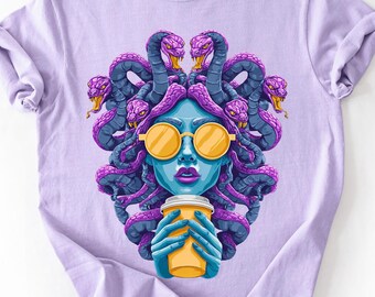 May include: A light purple t-shirt featuring a graphic of a Medusa-like figure with blue skin, purple hair of snakes, and yellow sunglasses. The figure holds a yellow coffee cup. The shirt is made of a soft material.