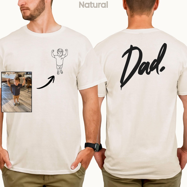 May include: A natural-colored t-shirt featuring a black line-art illustration of a child flexing on the front left chest. The back of the shirt displays the word "Dad." in large, black, brush-style script lettering. A small inset photo shows a child.
