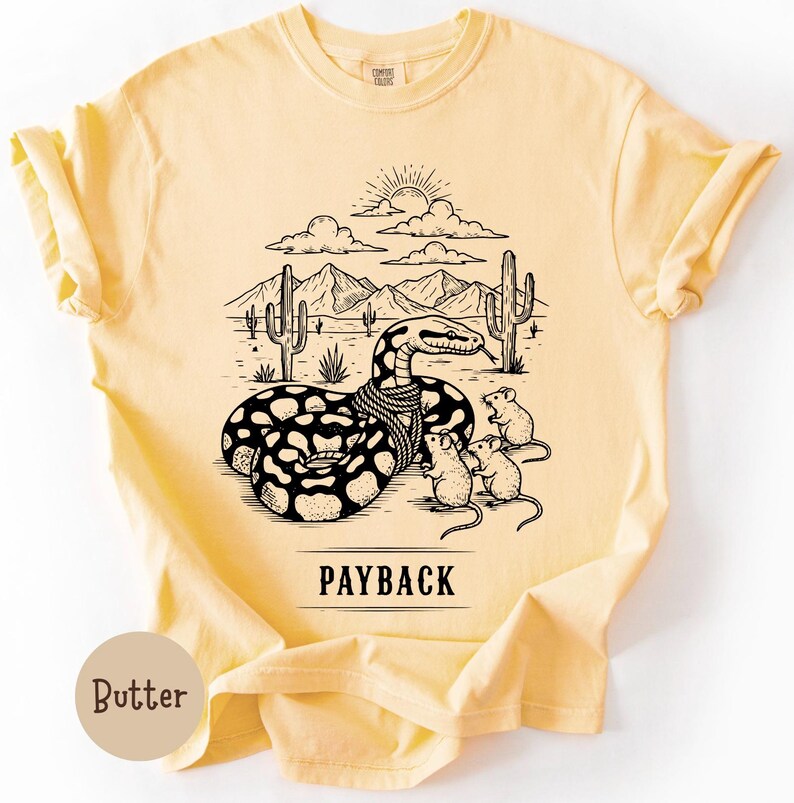 May include: Pale yellow t-shirt featuring a black and white graphic of a snake in a desert scene, with the word "PAYBACK" underneath. The snake has a rope around its neck, and is surrounded by cacti, mountains, and three mice.