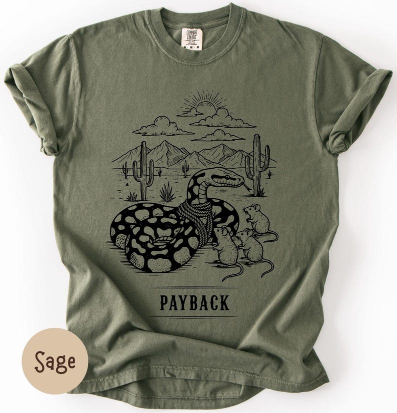 May include: Sage green t-shirt featuring a black graphic of a snake in a desert scene with cacti, mountains, and clouds. Three mice are near the snake. The word "PAYBACK" is printed below the graphic.