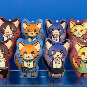 May include: Eight plush toys shaped like cats, each with a different color and design. The cats are wearing different outfits, including a sailor uniform, a school uniform, and a dress. The toys are all facing forward and have a friendly expression.