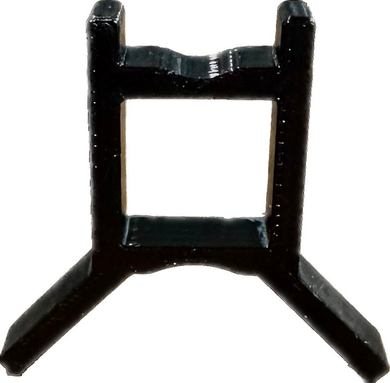 May include: A black plastic stand with a square opening in the center and three legs. The stand is designed to hold a small object.
