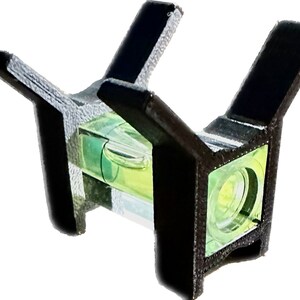 May include: A black plastic level with two arms extending out. The level has a clear glass tube with a green liquid inside. The level is designed to be used for checking if a surface is level.