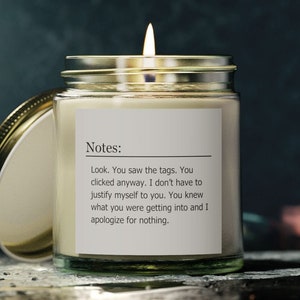 May include: A glass candle jar with a gold lid. The candle is lit and the jar has a white label with the text "Notes: Look. You saw the tags. You clicked anyway. I don't have to justify myself to you. You knew what you were getting into and I apologize for nothing."