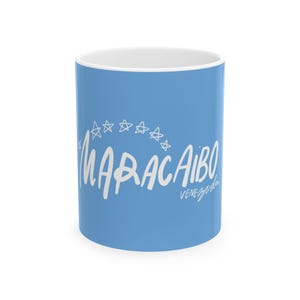 May include: A light blue ceramic mug featuring the word "MARACAIBO" in white script, arched above the word. The word "VENEZUELA" is written in white script below. The mug has a white interior.