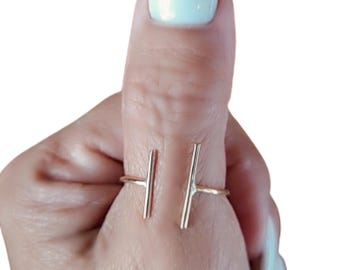 Puede incluir: Anillo abierto de color dorado con dos barras verticales como detalles. El anillo se lleva en un dedo con esmalte de uñas azul claro. El diseño minimalista y moderno del anillo es adecuado para el uso diario.