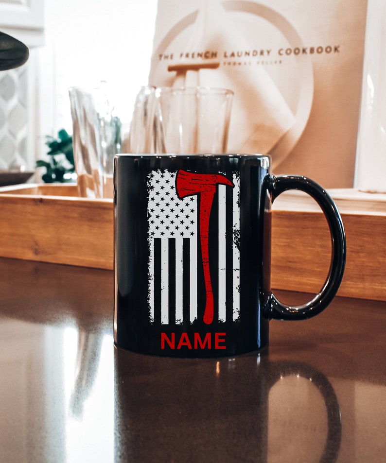 May include: Black ceramic mug with a white and red American flag design featuring a red axe. The text "NAME" is printed below the flag.