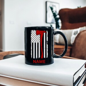 May include: Black ceramic mug featuring a red axe and an American flag design. The text "NAME" is printed on the bottom of the mug.
