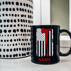 May include: Black coffee mug featuring a white and red American flag design with a red axe. The text "NAME" is printed on the bottom of the mug.
