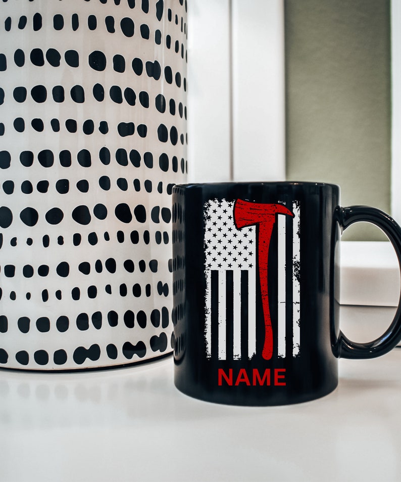 May include: Black coffee mug featuring a white and red American flag design with a red axe. The text "NAME" is printed on the bottom of the mug.
