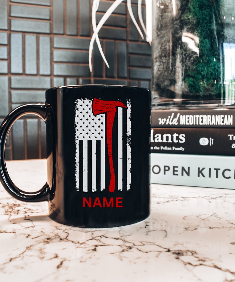 May include: Black ceramic coffee mug featuring a white and red American flag design with a red axe graphic. The text "NAME" is printed on the mug.