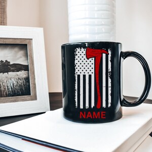 May include: Black ceramic coffee mug featuring a red and white American flag design with a red axe graphic. The text "NAME" is printed on the bottom of the mug.