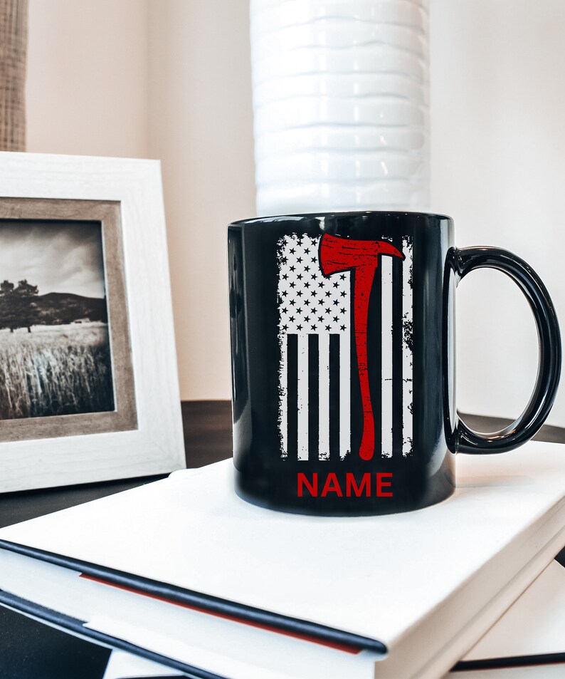 May include: Black ceramic coffee mug featuring a red and white American flag design with a red axe graphic. The text "NAME" is printed on the bottom of the mug.