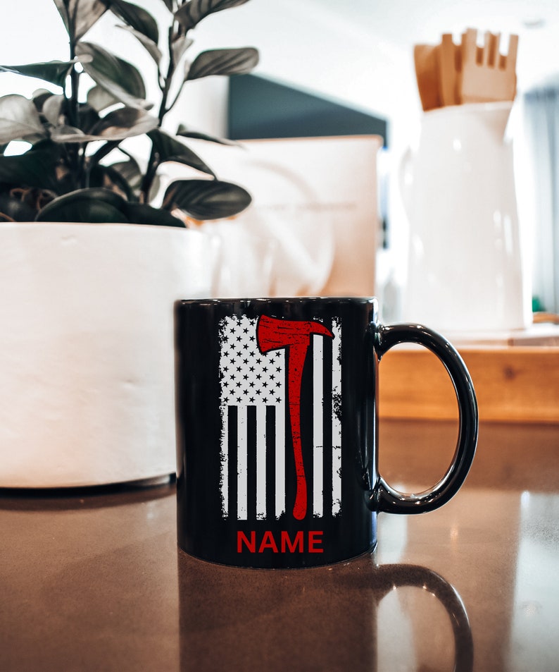 May include: Black ceramic mug featuring a white and red American flag design with a red axe graphic. The mug has white text that says "NAME" at the bottom.