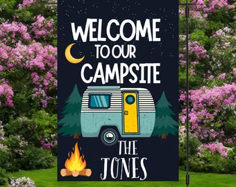 May include: A rectangular garden flag with a dark blue night sky background featuring a yellow crescent moon. The text reads WELCOME TO OUR CAMPSITE THE JONES. A light blue and yellow camper trailer sits between two green pine trees above a campfire.