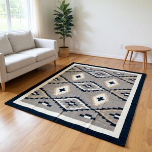 Top-down view of an 8x10 handwoven wool flatweave area rug with a grey, black, white, and tan Southwestern tribal geometric diamond pattern and a dark border on a light wood floor.