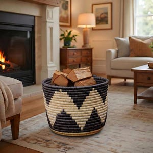 May include: A round woven basket with a black and cream geometric pattern, filled with firewood. The basket sits on a patterned rug in front of a fireplace with a burning fire.