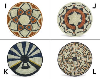 May include: Four round woven wall baskets labeled I, J, K, and L. Basket I has a geometric star pattern in rust, blue, and black. Basket J features a central rust ring with black and white accents. Basket K has blue and white rays. Basket L displays a complex black, white, and rust maze-like pattern.