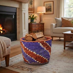 Peut inclure: Un panier rond tissé, orné de motifs géométriques violets, oranges et blancs, contient des bûches de bois. Le panier est posé sur un tapis à motifs devant une cheminée.