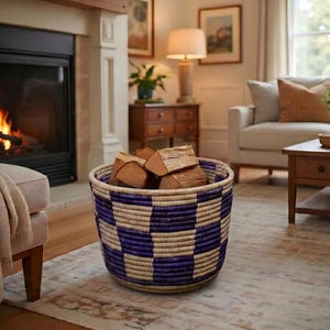 May include: A round, woven basket featuring a repeating checkerboard pattern in deep purple and natural beige tones. The basket is filled with several pieces of split firewood, showcasing a textured, hand-crafted appearance with a sturdy rim.