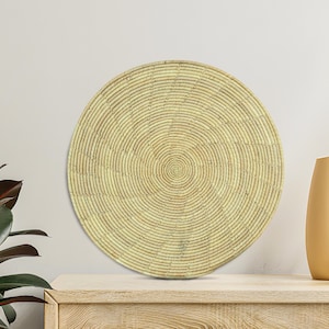 Op de afbeelding: Een ronde, geweven wandmand met een spiraalvormig ontwerp. De mand is gemaakt van natuurlijk gekleurde vezels en staat op een licht houten oppervlak. De mand heeft een diameter van ongeveer 61 cm.