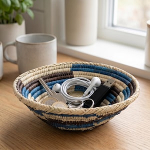 May include: A woven bowl with a geometric pattern in blue, brown, and natural tones. The bowl contains keys, earbuds, a USB drive, and other small items. The bowl sits on a wooden surface, suggesting a decorative storage solution.