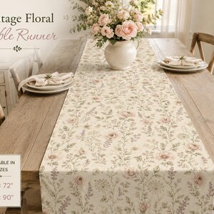 May include: A cream-colored table runner featuring a repeating floral pattern of pink roses and green foliage. The text on the image reads Vintage Floral Table Runner and Available in 2 sizes 16 inches by 72 inches and 16 inches by 90 inches.