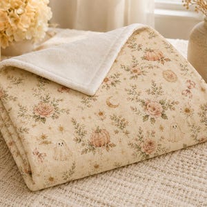 Folded velveteen blanket close-up showing soft plush texture, cream backing, detailed floral ghost pattern, and premium construction.