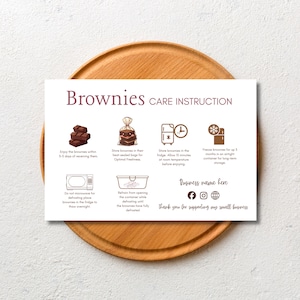 Puede incluir: Una tarjeta blanca con el texto "Brownies CARE INSTRUCTION", consejos de cuidado y un nombre comercial. Las instrucciones incluyen el almacenamiento, la congelación y la descongelación de los brownies. La tarjeta está sobre una bandeja de madera.