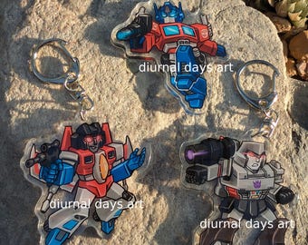 May include: Three clear acrylic keyrings featuring cartoon characters. One is red, white, and blue, another is red, white, blue, and black, and the third is grey, black, and purple. Each keyring has a silver ring and the text "diurnal days art".