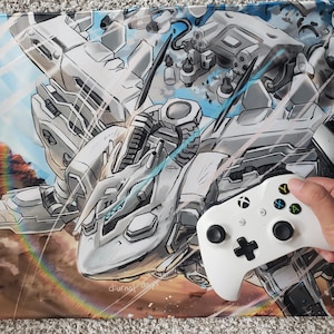 Könnte beinhalten: Ein weißer Gaming-Controller mit schwarzen Knöpfen und ein weiß-graues Anime-Mauspad mit einem Roboter im blau-weißen Design. Das Mauspad trägt den Text "diurnal days".
