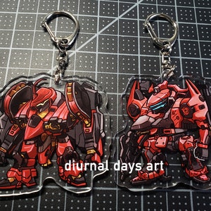 May include: Two red and black robot character keychains with silver keyrings. The keychains are made of clear acrylic and feature a cartoon style illustration of the robots.