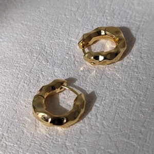 Puede incluir: Un par de pendientes de aro de oro con textura martillada. Los pendientes son simples y elegantes.